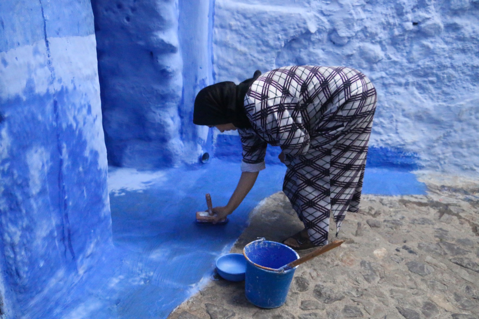 Solo traveller standing confidently with her phone on a blue street in Chefchaouen