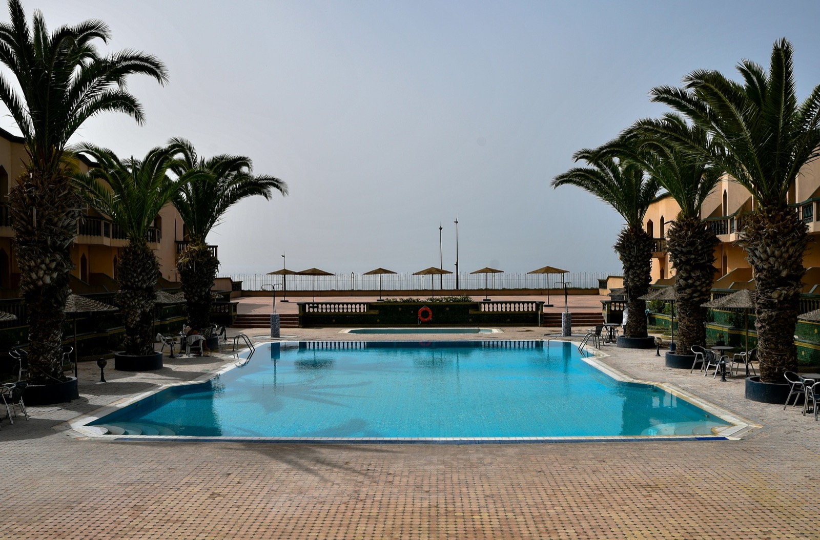 A resort pool with loungers and palm trees in the Marrakech Palmeraie on a summer afternoon